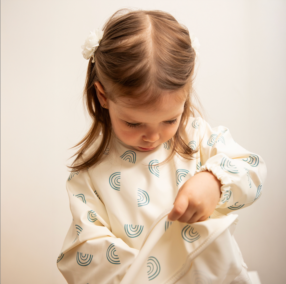 Niña usando pechera de aprendizaje impermeable con diseño de arcoíris, ideal para alimentación complementaria y juegos