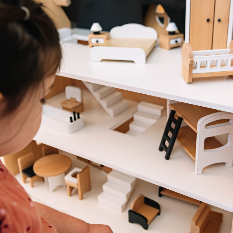 Niña jugando con casa de muñecas de tres pisos y muebles de madera.